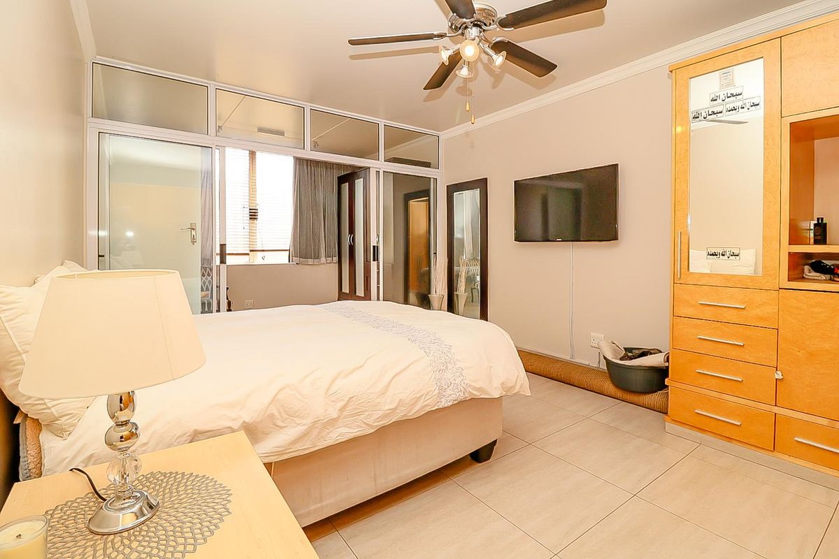 A bedroom featuring tiled flooring, a ceiling fan, and built-in cabinetry, with a glass partition wall providing natural light.