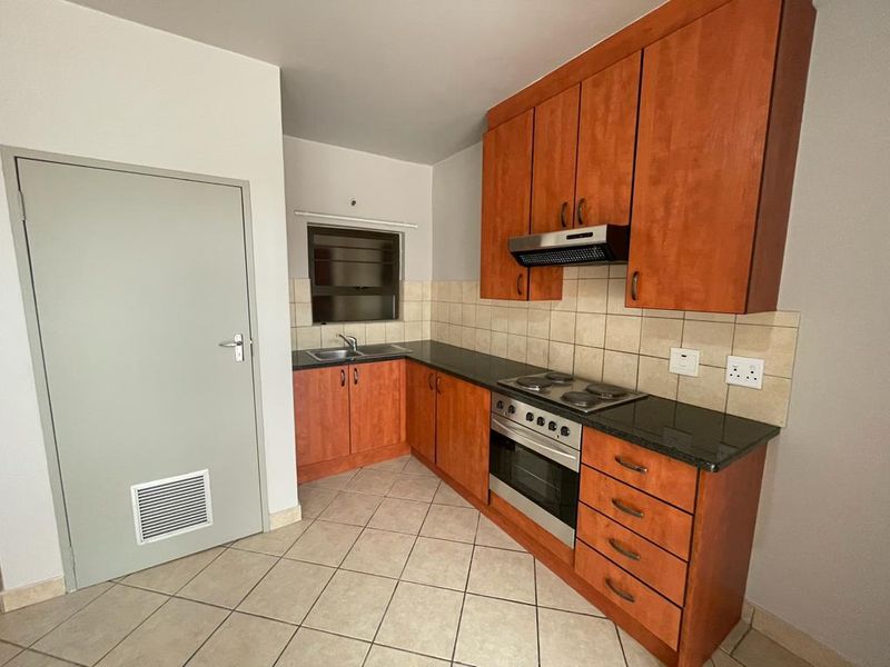 A functional kitchen featuring wooden cabinetry, granite countertops, built-in oven, electric hob, and tiled flooring.