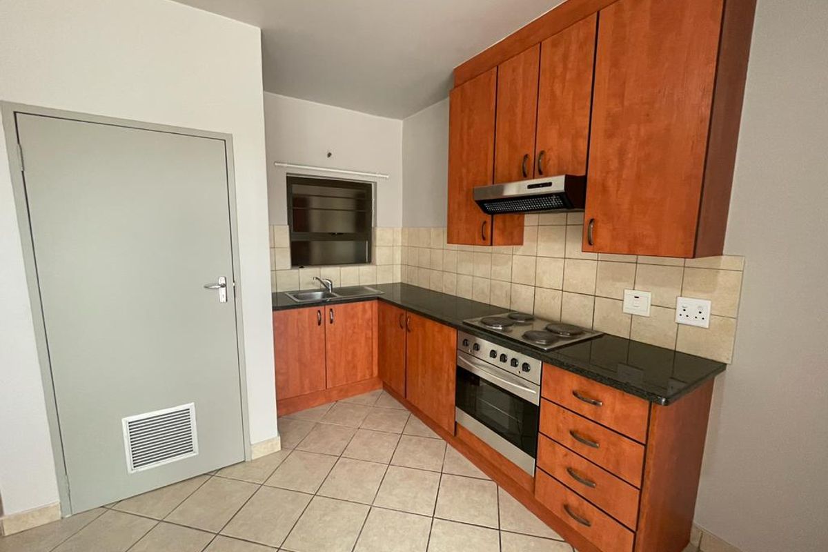 A functional kitchen featuring wooden cabinetry, granite countertops, built-in oven, electric hob, and tiled flooring.