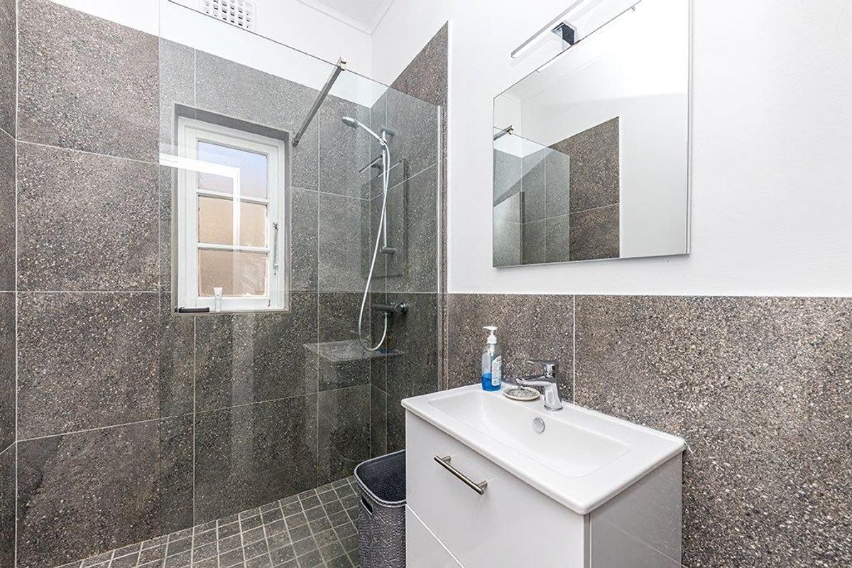 Modern bathroom featuring a glass-enclosed shower with dark stone-look tiling, a contemporary vanity with basin, and a wall-mounted mirror.