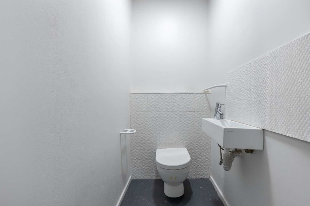 A compact, modern office restroom featuring a wall-mounted basin, a white toilet, and textured wall tiling.
