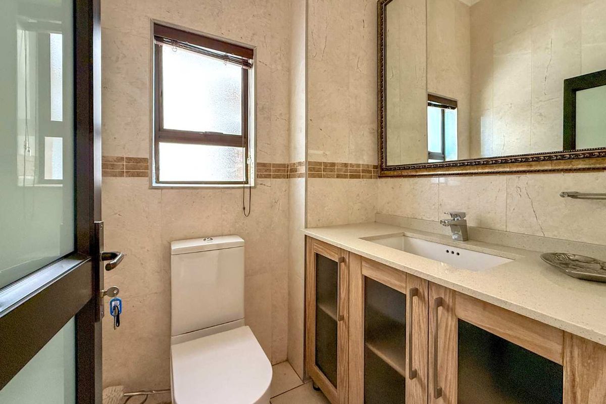 A well-maintained bathroom featuring a modern vanity with stone countertop, undermount sink, large wall mirror, and neutral floor-to-ceiling wall tiles.