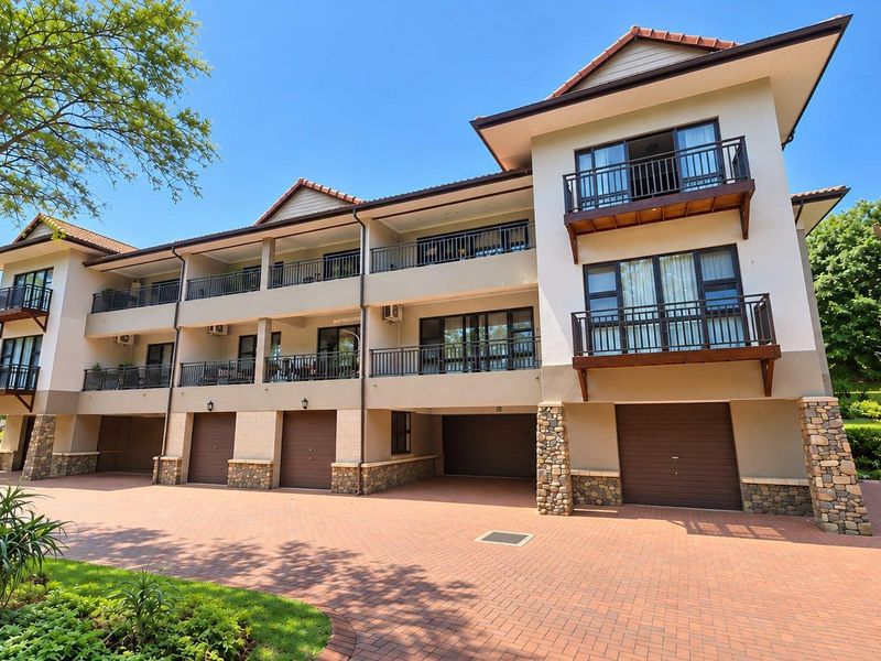 A well-maintained multi-story apartment complex featuring brick paving, stone accents, private balconies with metal railings, and integrated ground-level garage access.