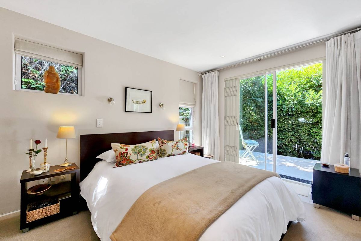 Bright bedroom featuring neutral walls, carpeted flooring, and large sliding glass doors providing direct access to a private outdoor patio area.
