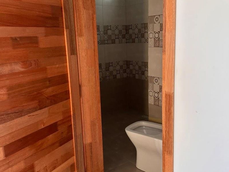 A view into a small bathroom featuring tiled walls and a standard toilet, accessed through a wooden door frame.
