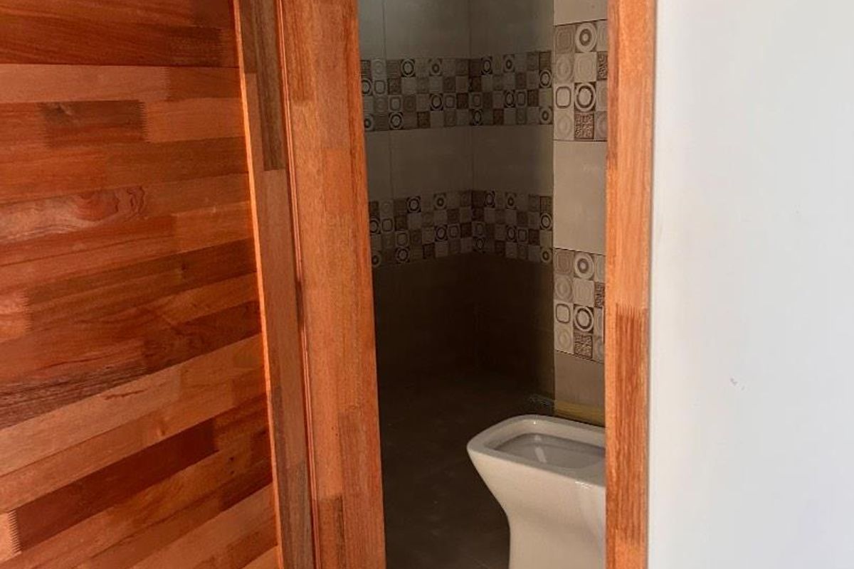 A view into a small bathroom featuring tiled walls and a standard toilet, accessed through a wooden door frame.