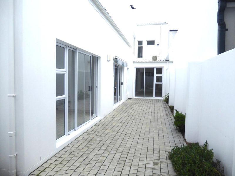 A clean, paved rear courtyard area featuring white exterior walls and multiple sliding glass door access points to the home.