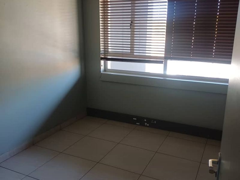 A vacant office space featuring tiled flooring, a suspended ceiling, and fitted venetian blinds with integrated power skirting for connectivity.