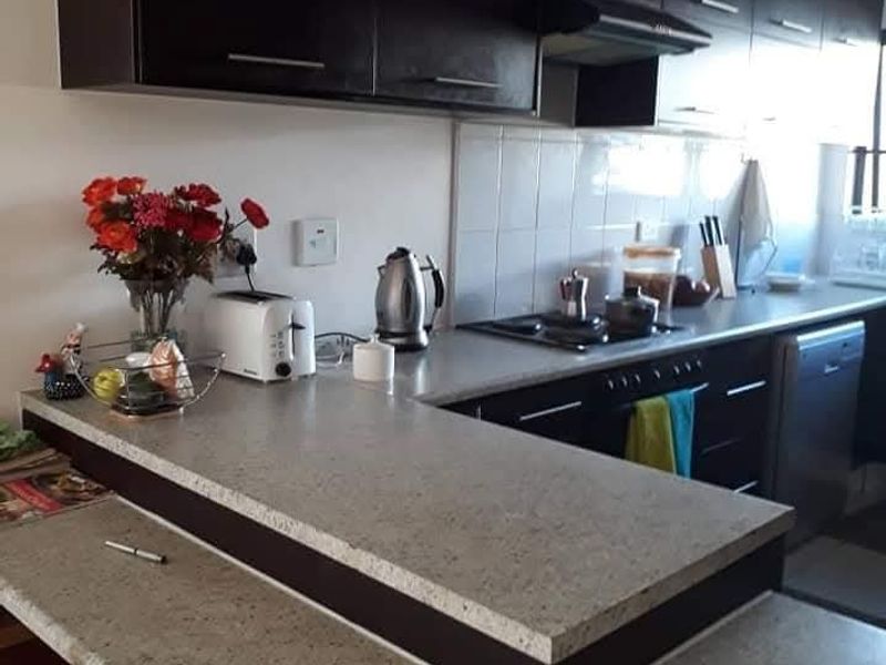 A functional kitchen featuring dark cabinetry, stone-look countertops, a breakfast bar, and a tiled backsplash with integrated hob and extractor fan.