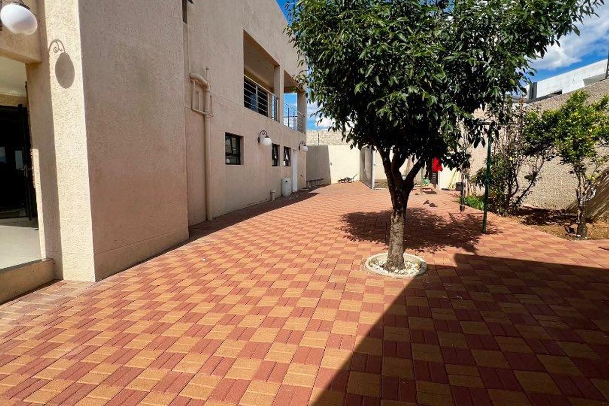 A spacious rear courtyard featuring paved brick flooring, a mature tree, and direct access to the side of the house.