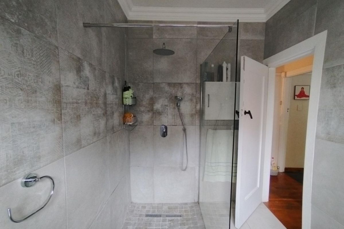 Modern bathroom featuring a spacious walk-in shower with glass screen, rainfall shower head, and contemporary grey wall tiling.