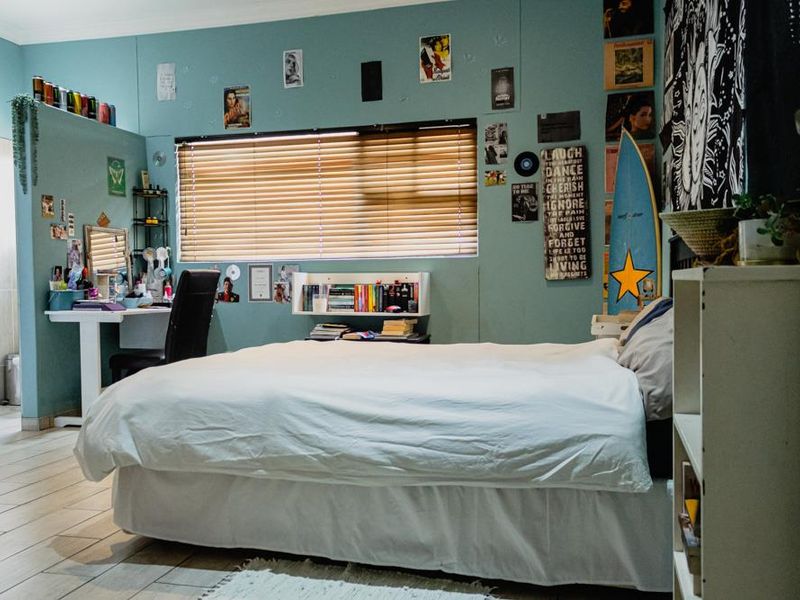 A bedroom featuring tiled flooring, a built-in desk area, and a window with fitted blinds.