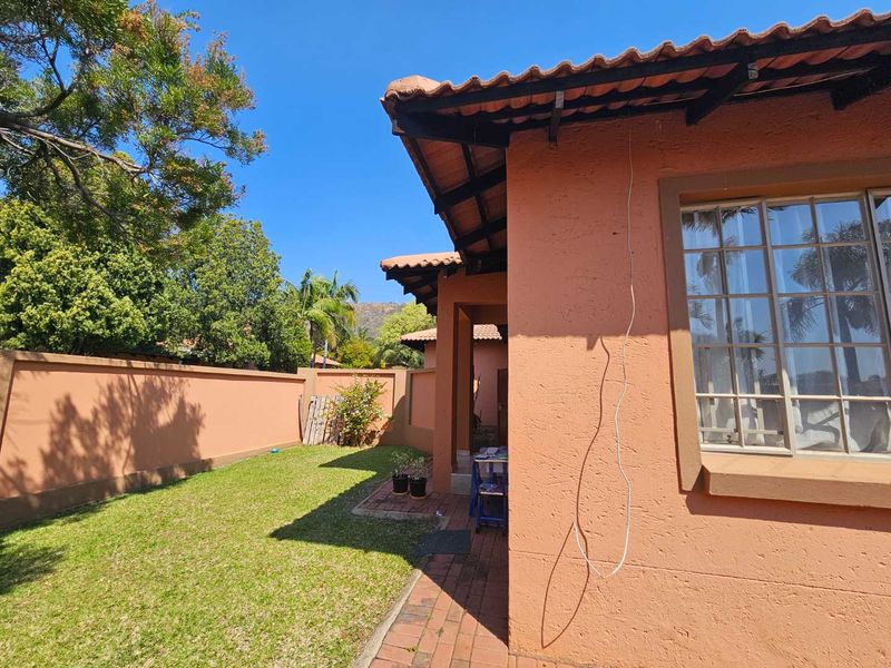 Rear exterior view of the house featuring a terracotta tiled roof, brick paved walkway, and a private garden area enclosed by a boundary wall.