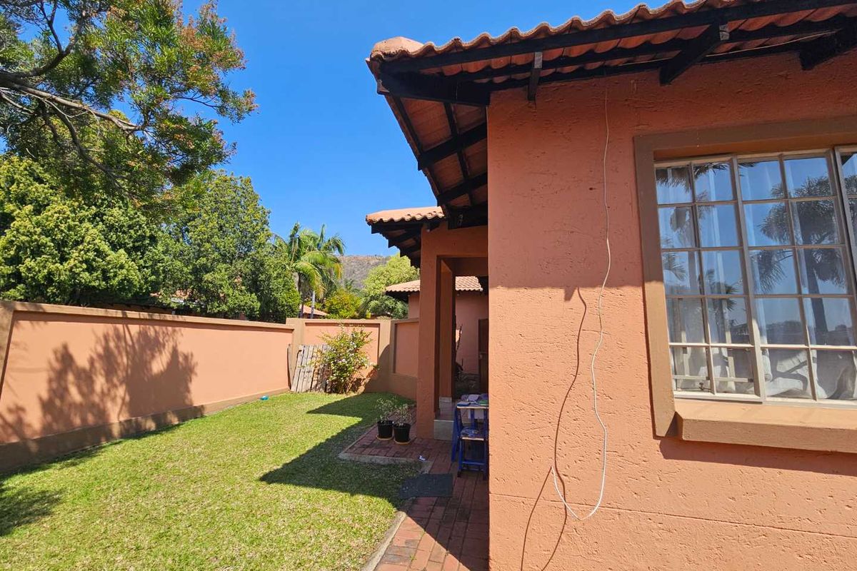 Rear exterior view of the house featuring a terracotta tiled roof, brick paved walkway, and a private garden area enclosed by a boundary wall.