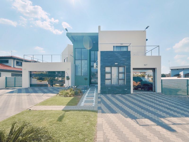 Modern double-story residential facade featuring a paved driveway, double garage, stone-clad accents, and an upper-level balcony.