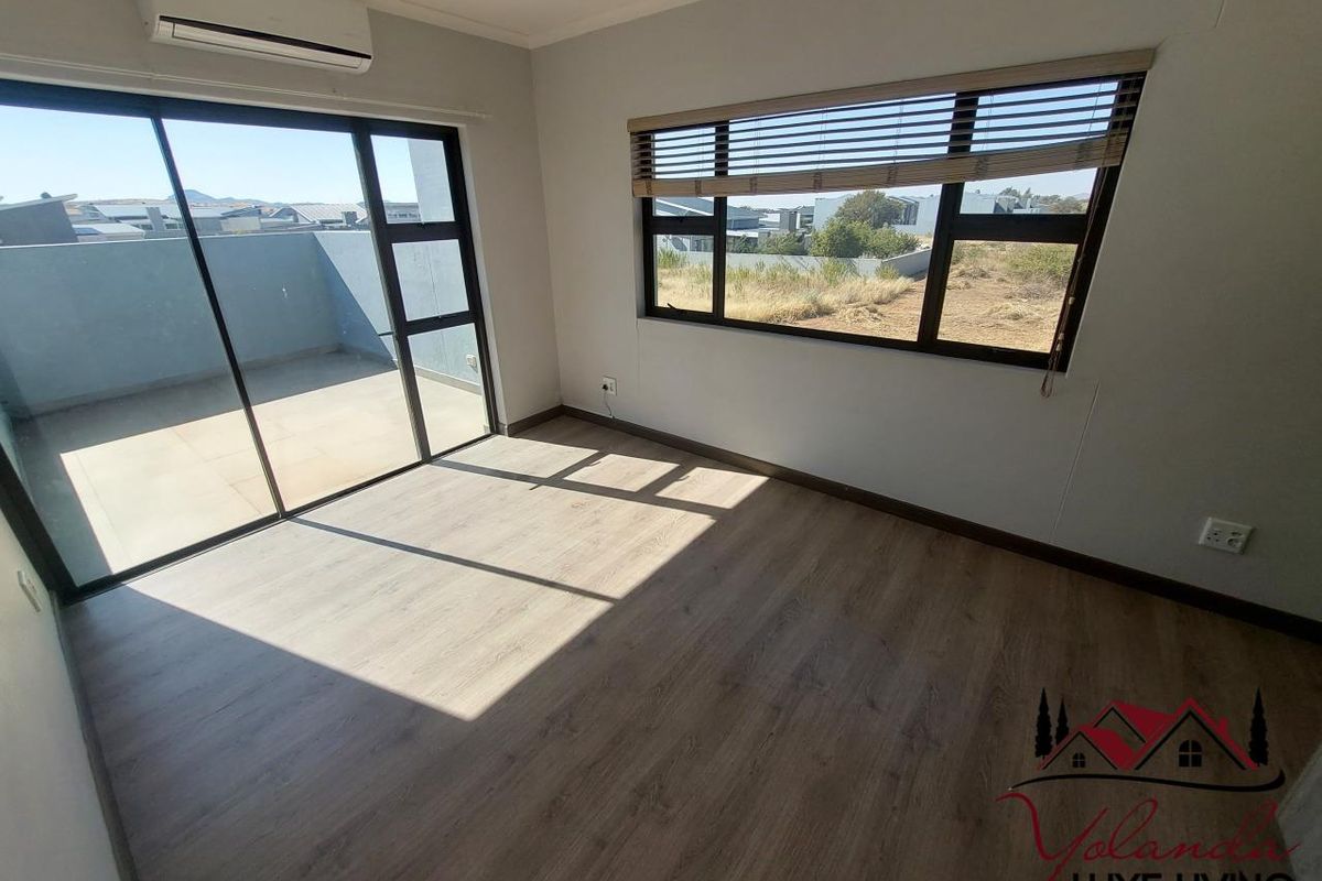 A bright, empty bedroom featuring modern laminate flooring, a split-system air conditioner, and large sliding glass doors leading to an outdoor balcony area.