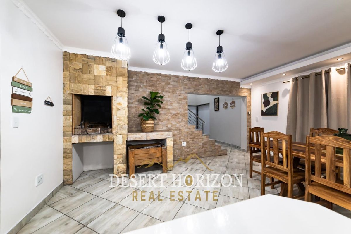 Living area featuring a prominent stone-clad built-in braai, tiled flooring, and modern pendant lighting, creating a warm and inviting space.