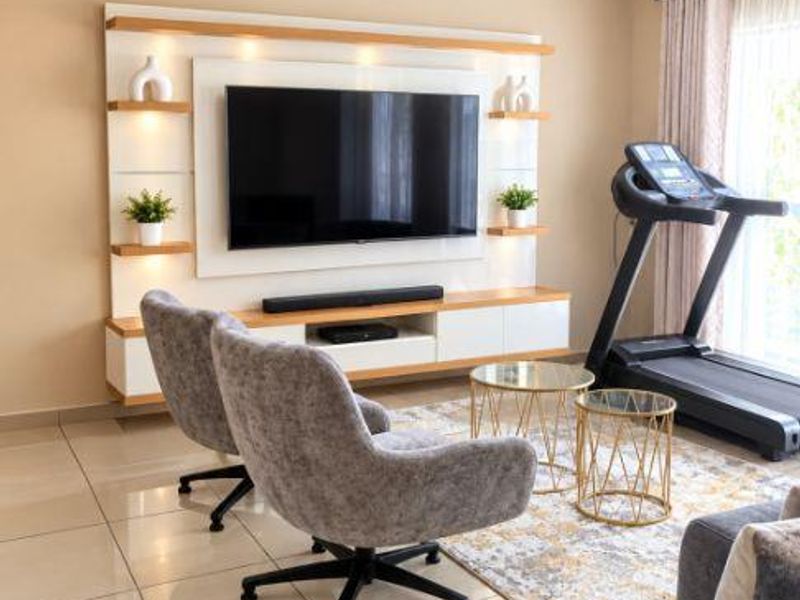 A well-maintained living room featuring a modern built-in media unit with integrated shelving and recessed lighting, complemented by neutral tiled flooring.