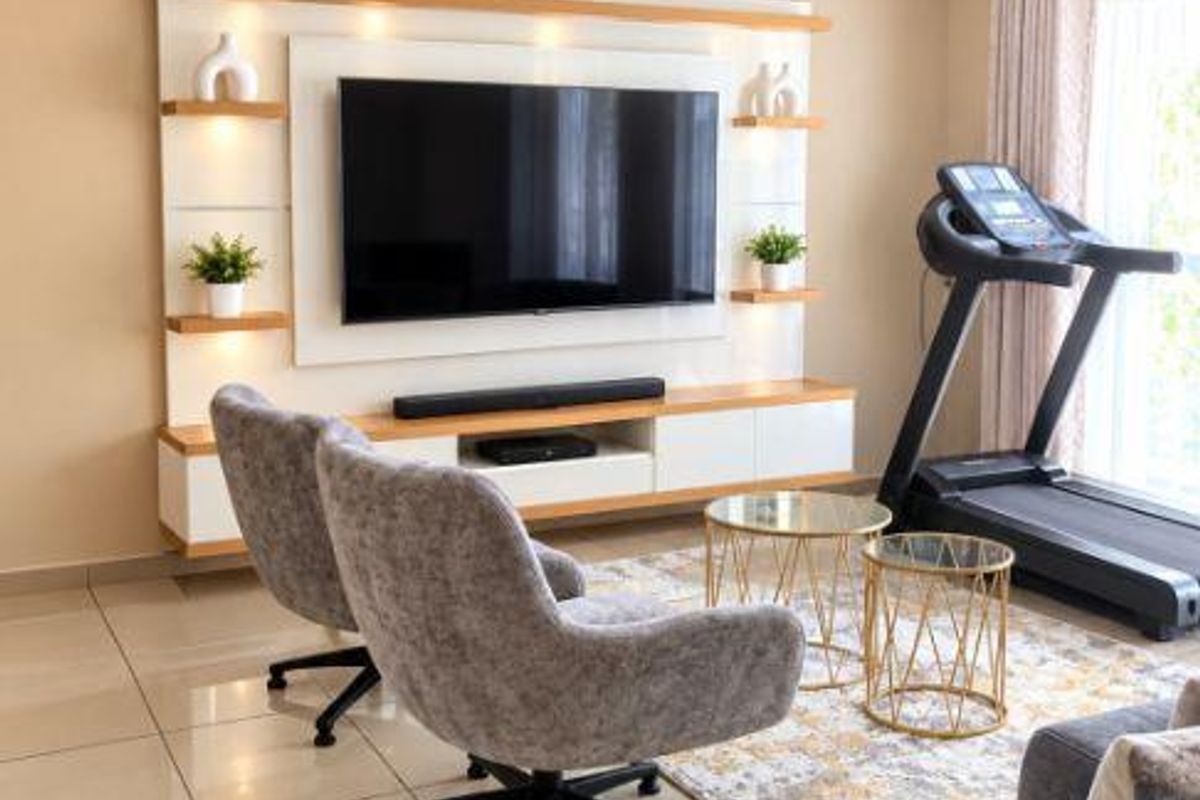 A well-maintained living room featuring a modern built-in media unit with integrated shelving and recessed lighting, complemented by neutral tiled flooring.