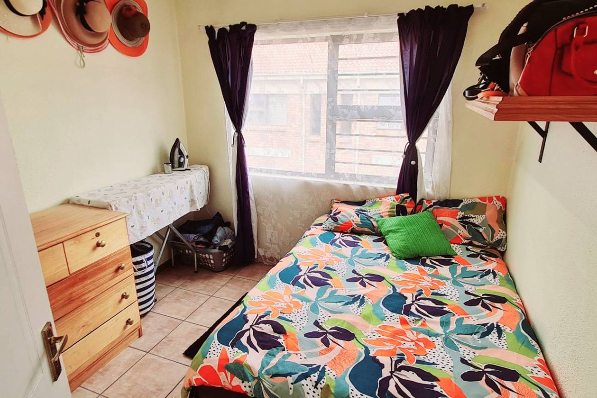 A compact bedroom featuring tiled flooring and a window with security bars, providing a functional space for a single bed.