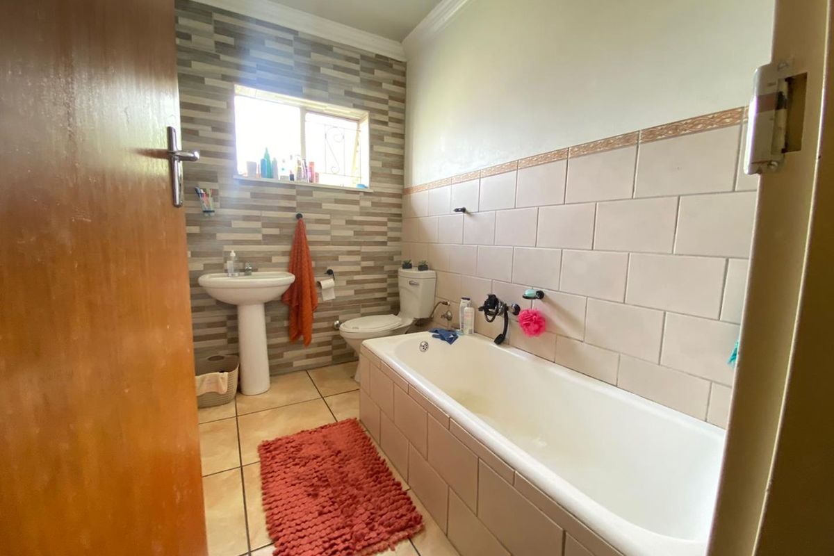 A functional bathroom featuring a built-in bathtub, pedestal washbasin, toilet, and neutral tiled finishes with a decorative accent wall.