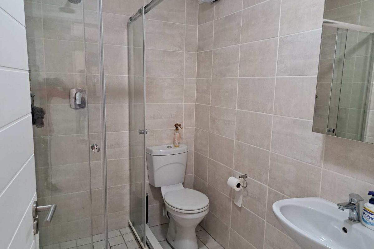 A clean, modern bathroom featuring a glass-enclosed shower, pedestal basin, and wall-mounted toilet with neutral floor-to-ceiling tiling.