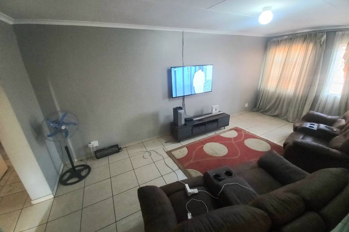 A living room featuring tiled flooring, neutral wall paint, and large windows with curtains, providing a functional and comfortable living space.