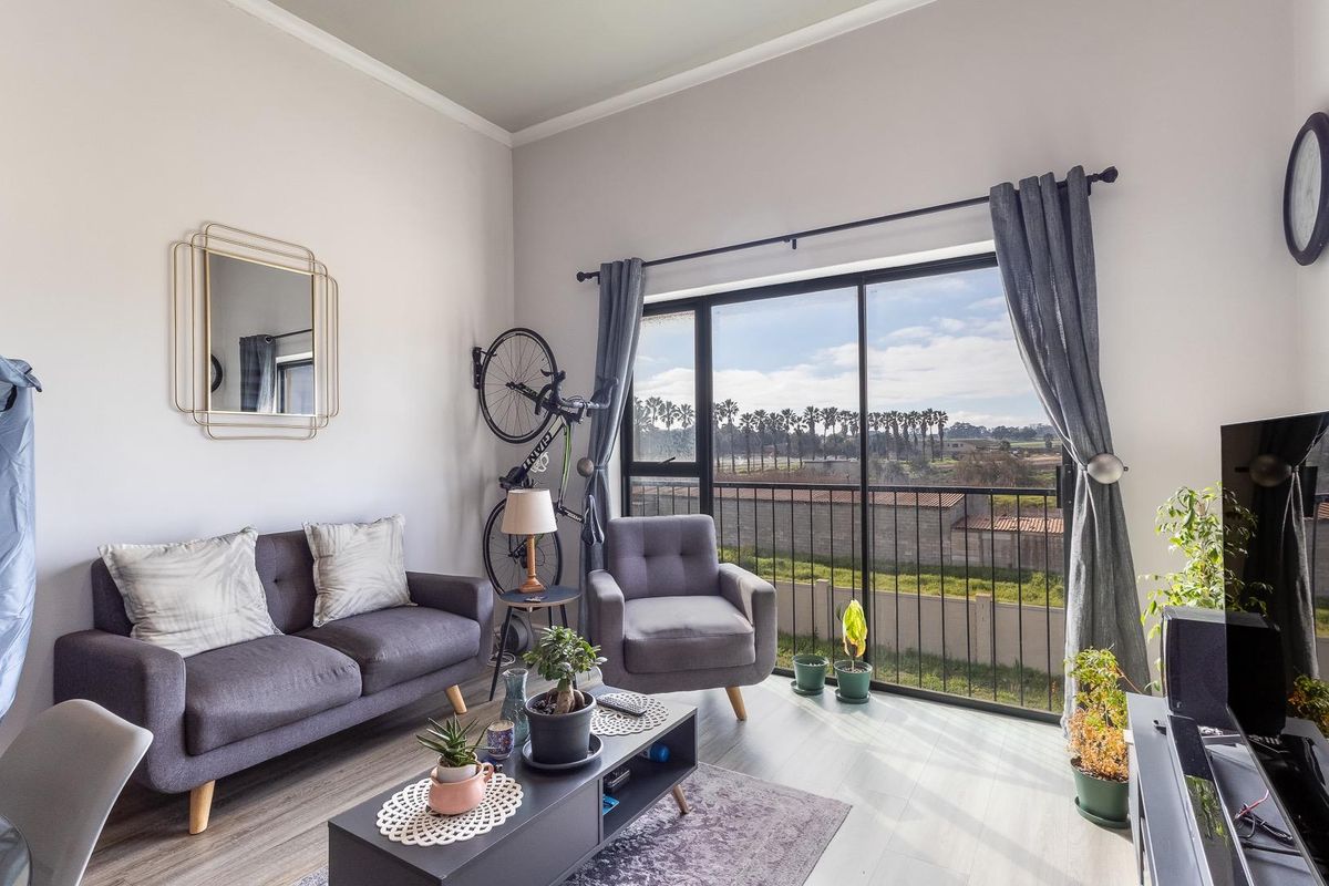 A bright living room featuring laminate flooring, coving, and a large sliding glass door that opens onto a balcony with scenic views.