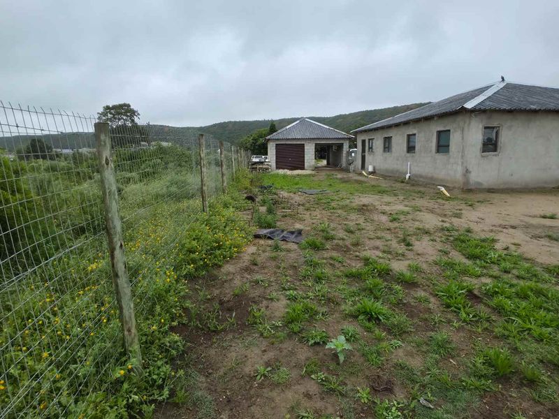 Rear view of the property featuring an unfinished concrete block house, detached garage, and wire mesh perimeter fencing on a large unlandscaped plot.