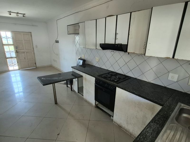 Open plan kitchen and living area featuring granite countertops, built-in oven, hob, and tiled flooring, requiring cosmetic updates and repairs.