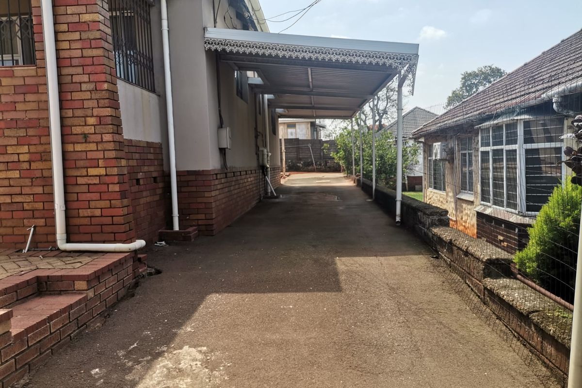 A side driveway area featuring a covered carport structure, brick masonry, and paved surfaces between two residential buildings.