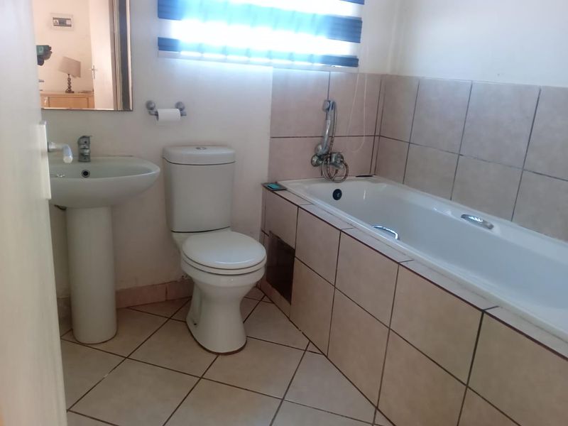A functional bathroom featuring a pedestal basin, toilet, and a tiled bathtub with a shower mixer, finished with neutral wall and floor tiles.