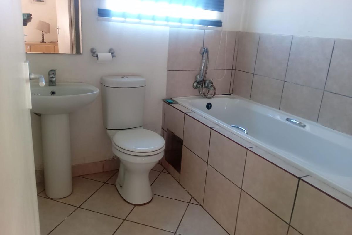 A functional bathroom featuring a pedestal basin, toilet, and a tiled bathtub with a shower mixer, finished with neutral wall and floor tiles.
