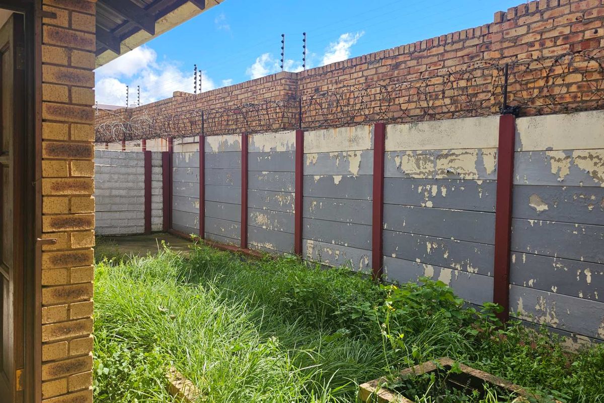 A rear exterior view of the property featuring a private garden area enclosed by a high boundary wall with security fencing.