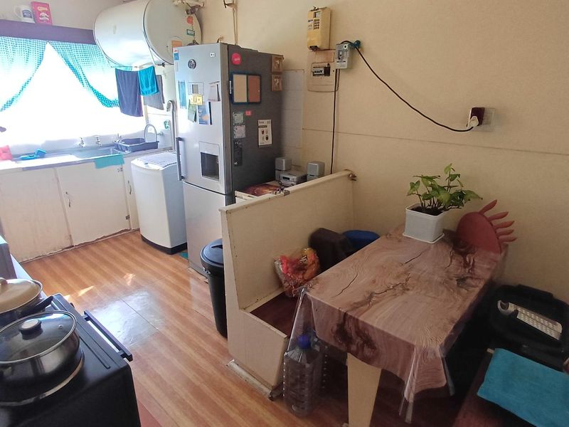 A compact kitchen featuring basic cabinetry, a sink, and an electric water heater, with visible electrical wiring and dated finishes.