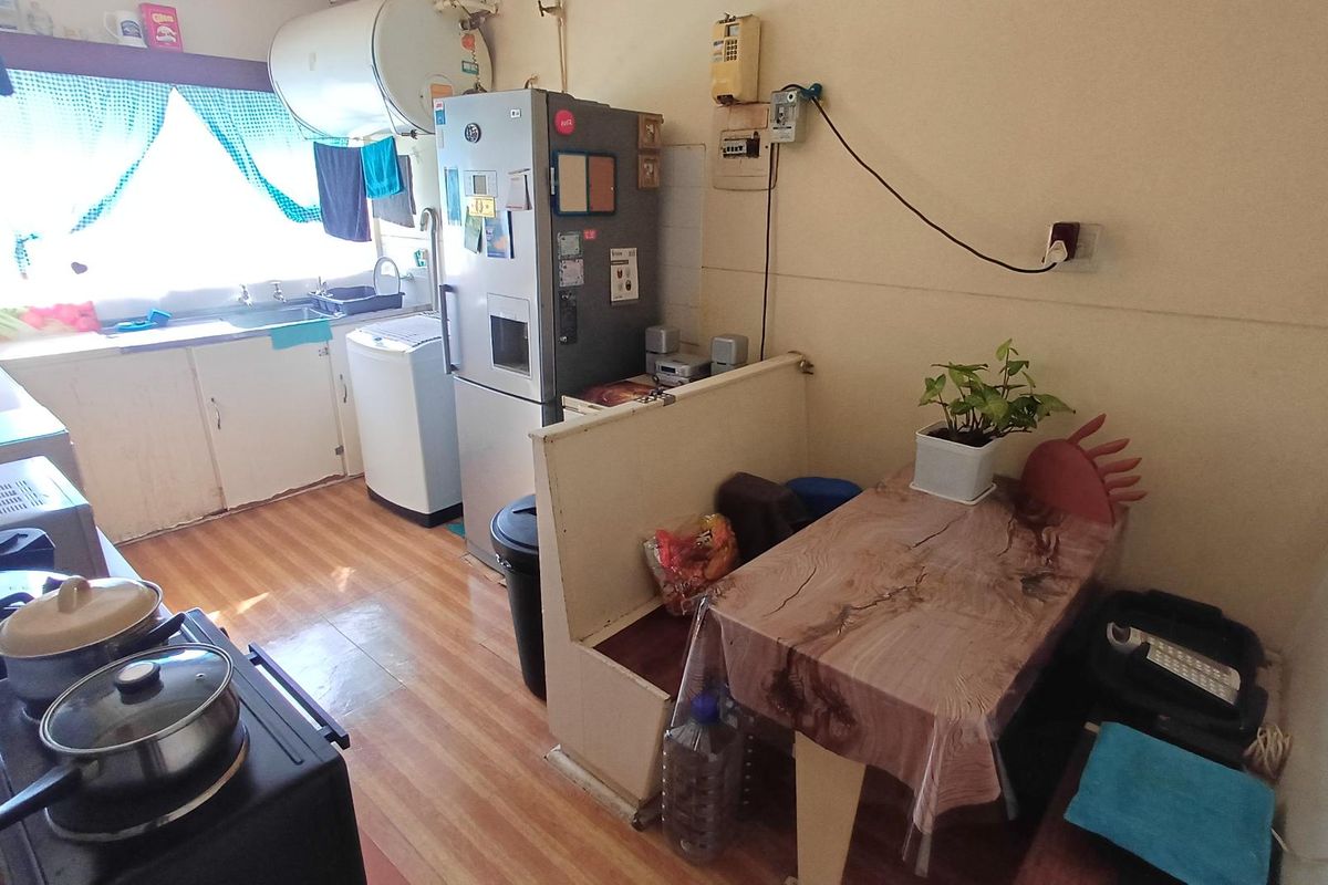 A compact kitchen featuring basic cabinetry, a sink, and an electric water heater, with visible electrical wiring and dated finishes.