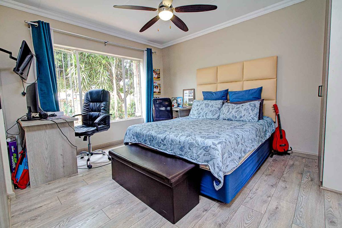 A well-lit bedroom featuring wood-look laminate flooring, a ceiling fan, and large windows with security bars, providing a functional and comfortable living space.