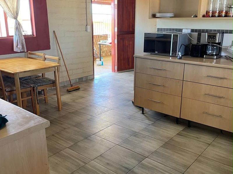 A functional kitchen area featuring tiled flooring, built-in cabinetry, and exposed ceiling beams, with direct access to an outdoor space.