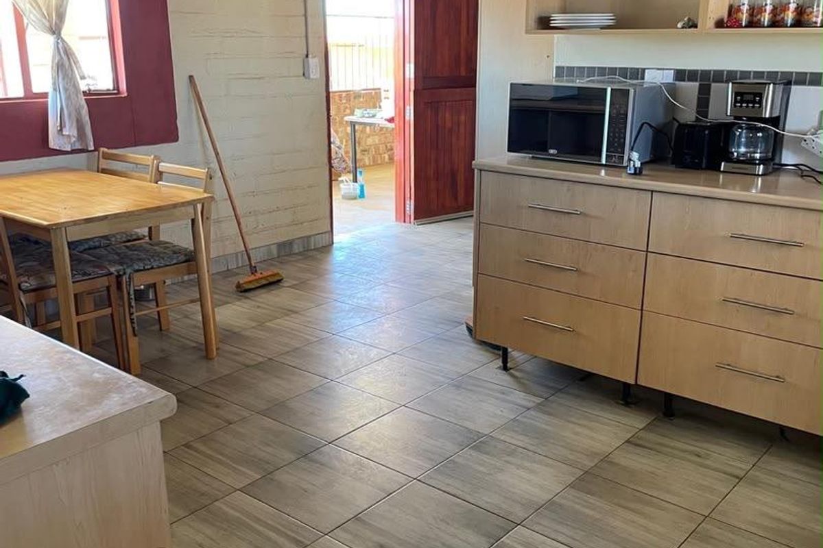 A functional kitchen area featuring tiled flooring, built-in cabinetry, and exposed ceiling beams, with direct access to an outdoor space.