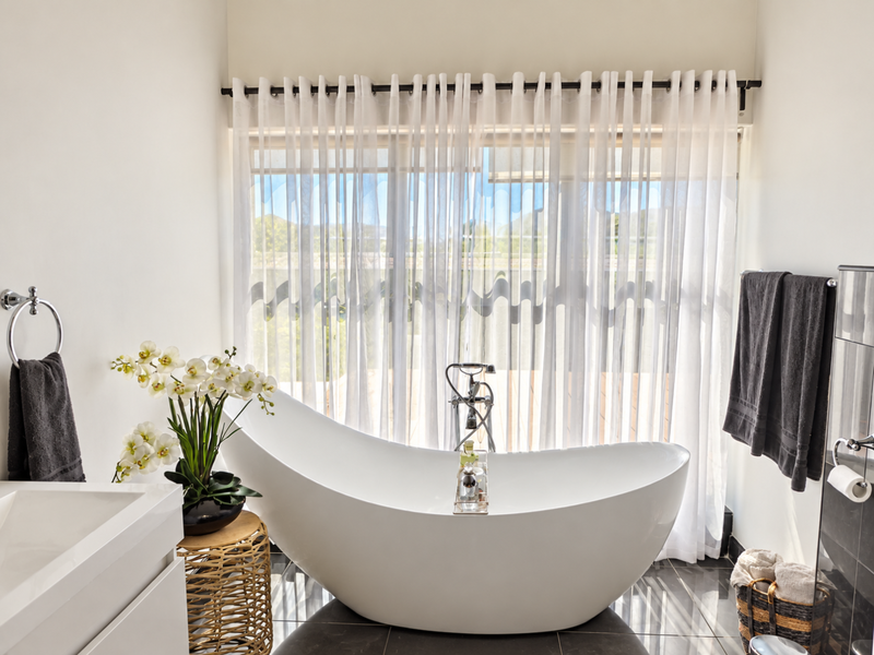 Modern bathroom featuring a sleek freestanding bathtub, floor-mounted faucet, and large window with sheer curtains, creating a bright and tranquil space.