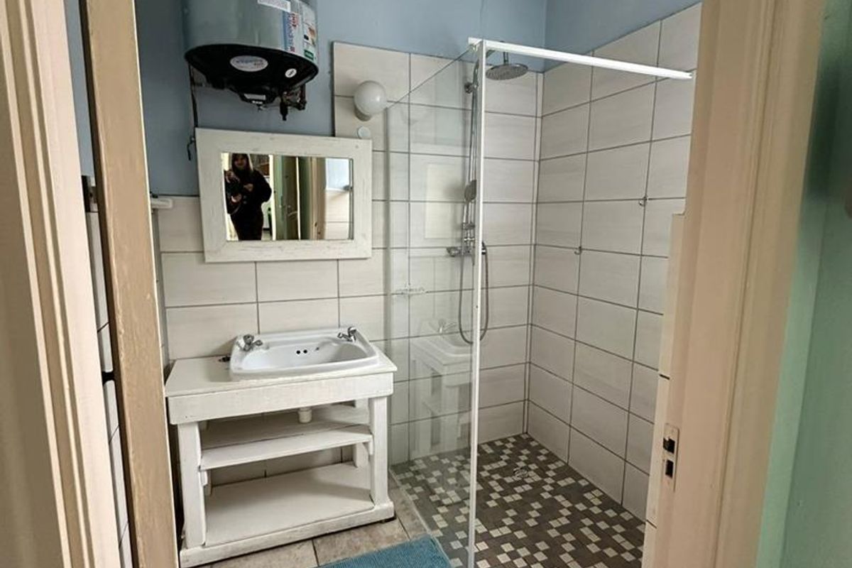 A functional bathroom featuring a walk-in shower with glass screen, pedestal-style vanity, and an exposed wall-mounted electric water heater.