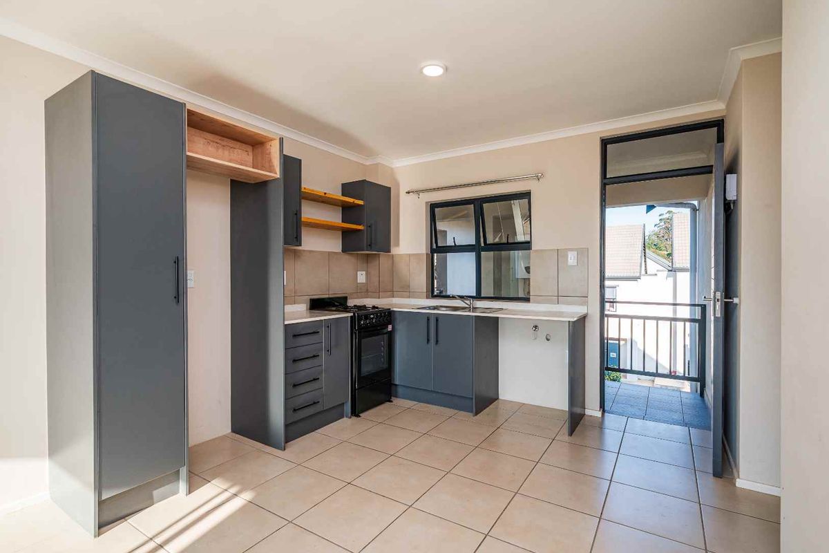 A clean, functional kitchen featuring dark grey cabinetry, a freestanding stove, tiled flooring, and direct access to an outdoor balcony area.