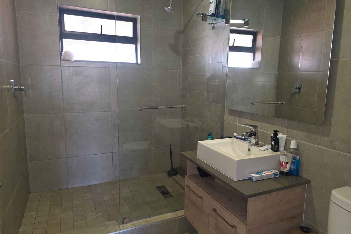 Modern bathroom featuring a walk-in shower with glass screen, vanity cabinet with countertop basin, and large wall mirror.