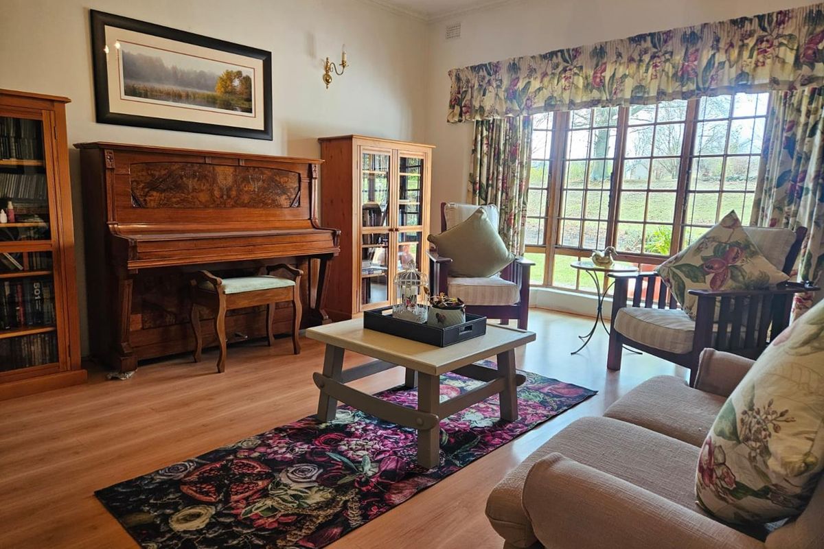 A comfortable living room featuring large timber-framed windows, laminate flooring, and decorative ceiling cornicing, offering a bright and inviting space.