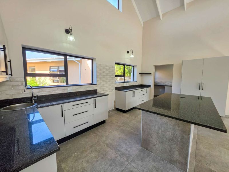 Modern kitchen featuring granite countertops, a central island, subway tile backsplash, and high vaulted ceilings with exposed rafters, offering a bright and spacious layout.