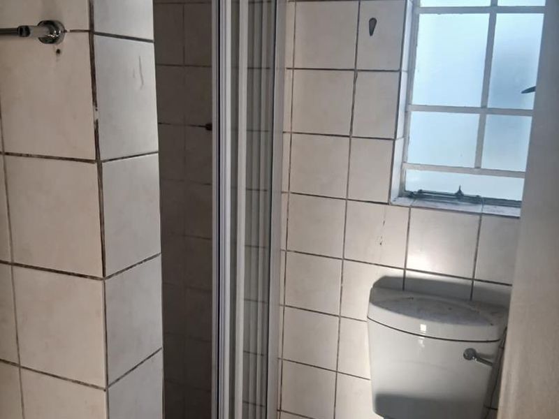 A compact bathroom featuring a shower enclosure, toilet, and tiled wall finishes, requiring some maintenance and cosmetic updates.