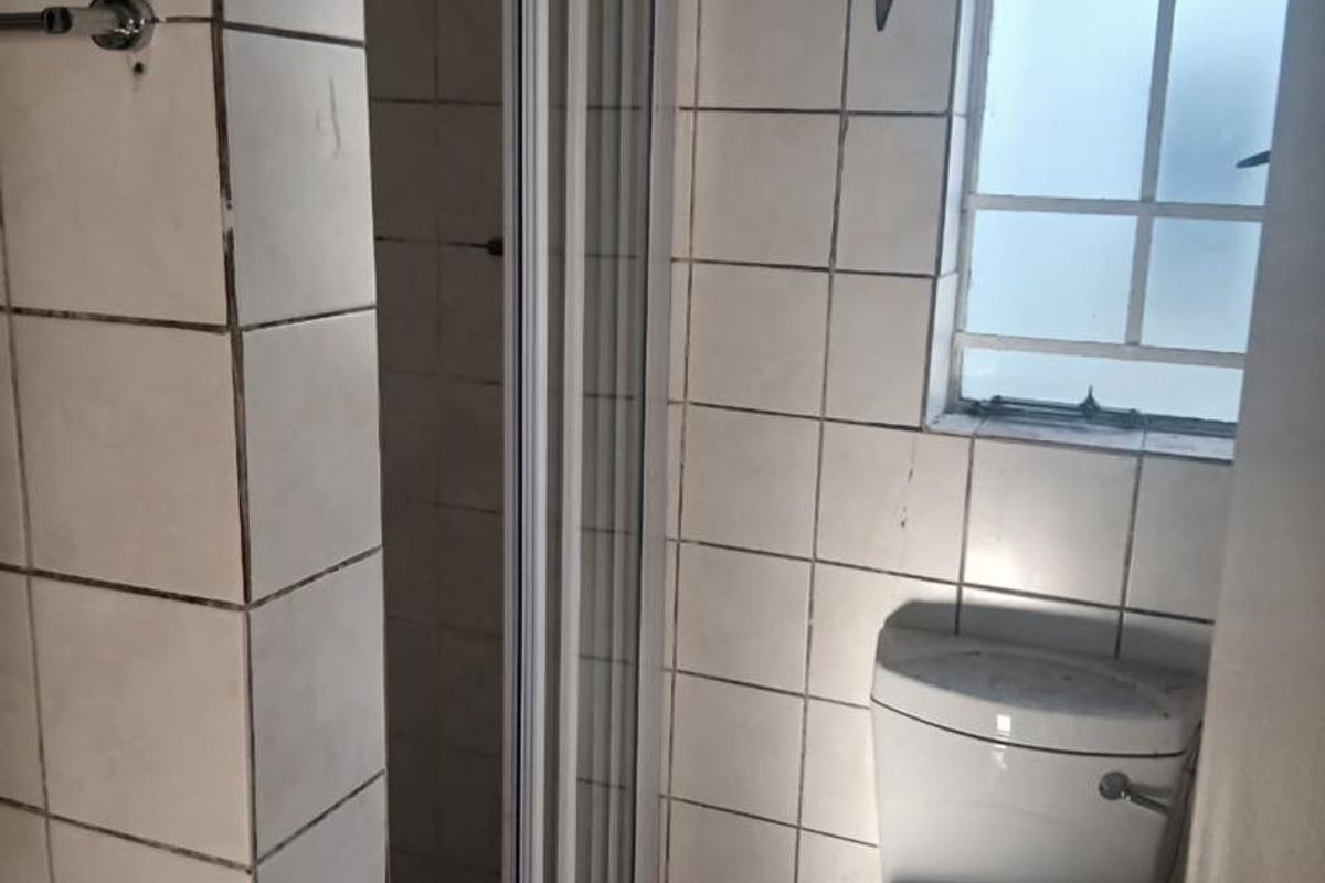 A compact bathroom featuring a shower enclosure, toilet, and tiled wall finishes, requiring some maintenance and cosmetic updates.