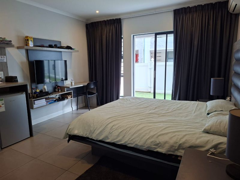 A well-maintained bedroom featuring tiled flooring, a built-in desk and shelving unit, and a sliding glass door providing access to the exterior.