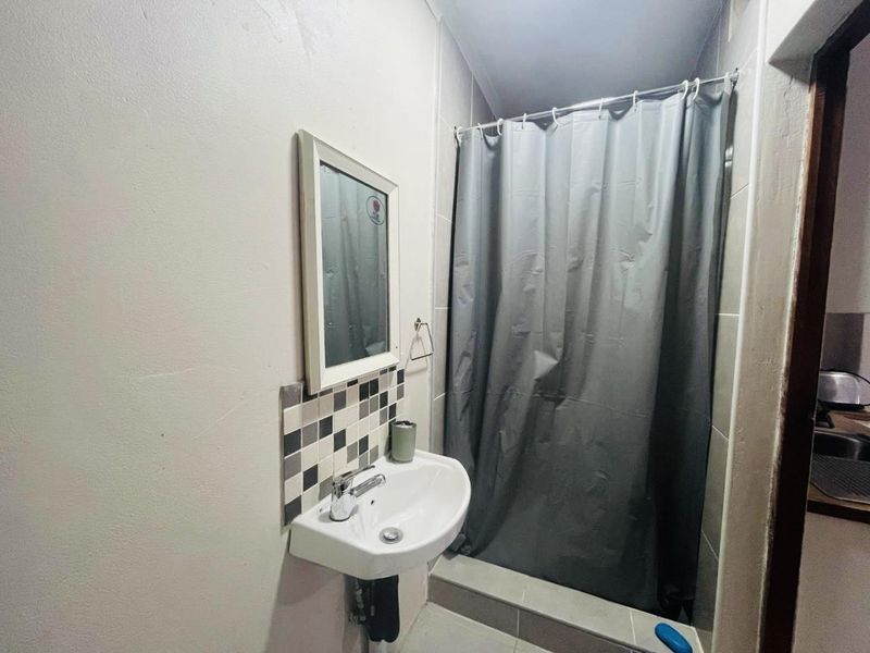 Compact bathroom featuring a wall-mounted basin with tiled splashback and a shower area with a curtain.