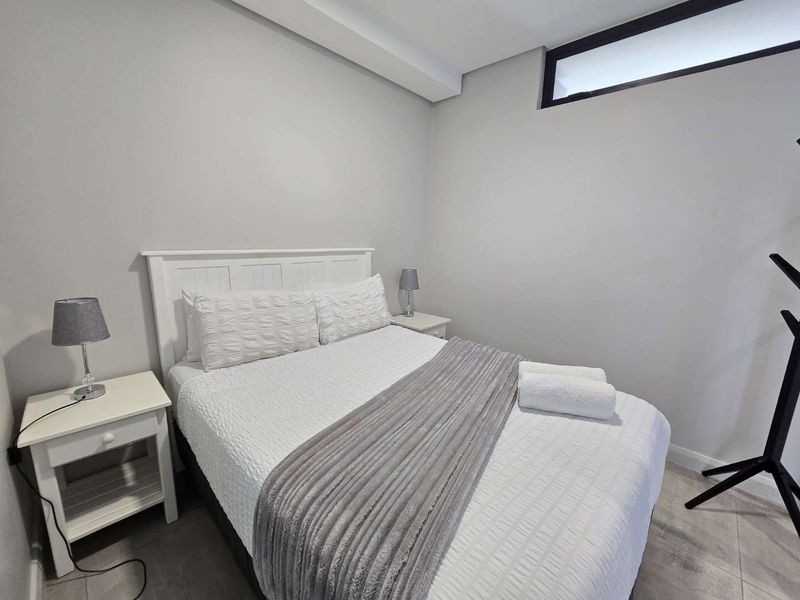 A well-maintained bedroom featuring neutral wall tones, tiled flooring, and a high-positioned clerestory window for natural light.